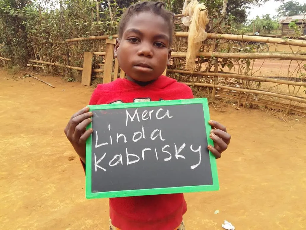 Une fillette tient une ardoise « Merci Linda Kabrisky »