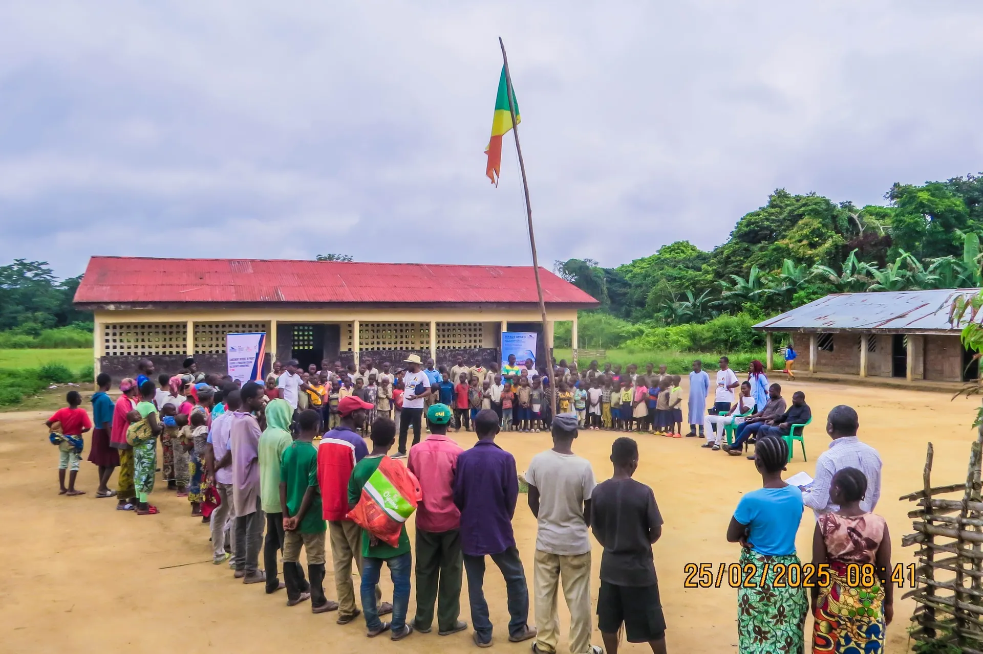 Rassemblement d’élèves devant une école, drapeau congolais au mât